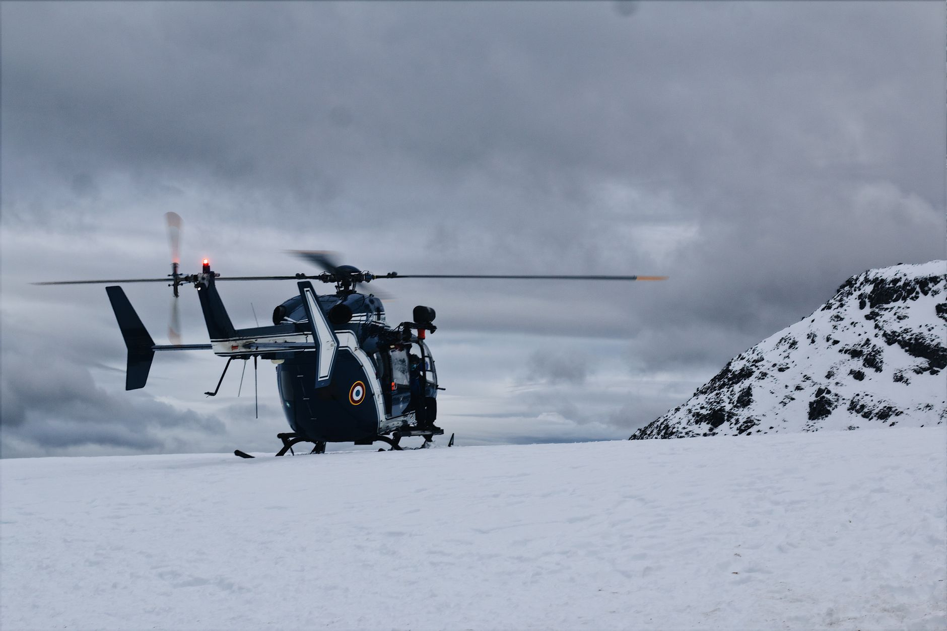 A helicopter lands in a snowy mountain setting under overcast skies, capturing winter's chill.