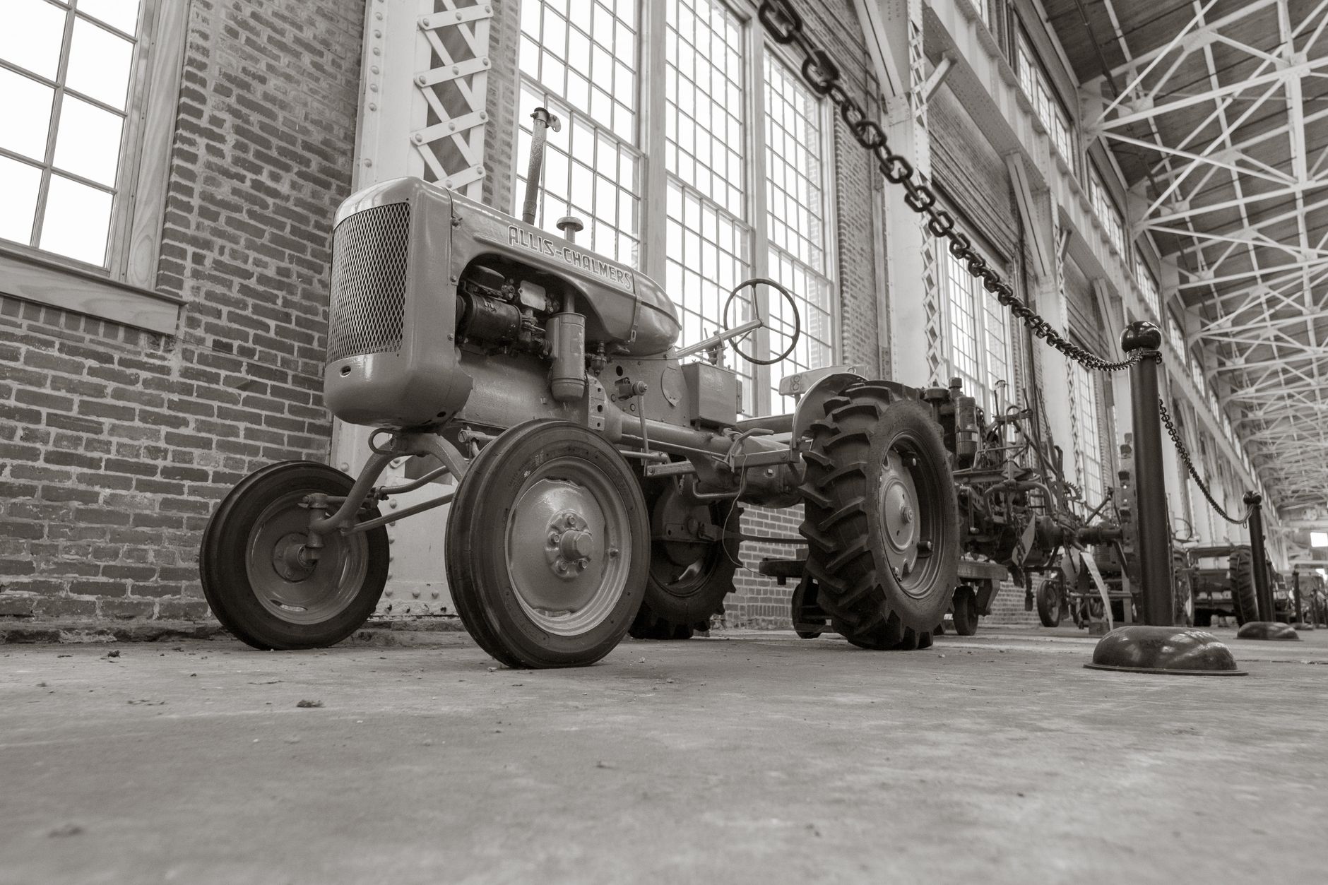 Black and white photo of a vintage Allis-Chalmers tractor displayed indoors in an industrial museum.