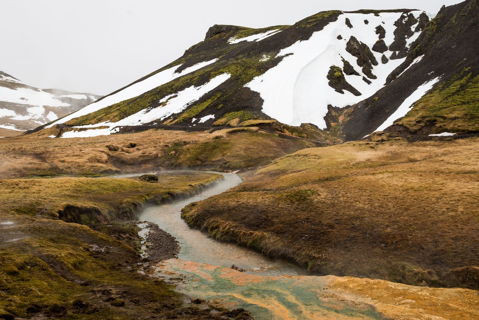A beautiful mountainous landscape with patches of snow and a meandering stream in spring.