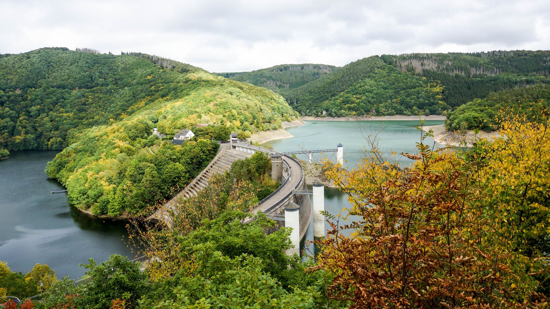 Beautiful view of a reservoir and dam surrounded by green hills and colorful autumn foliage.